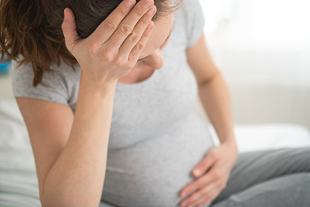 Gestante sentada e mostrando ansiedade, com uma mão na testa e outra na barriga.