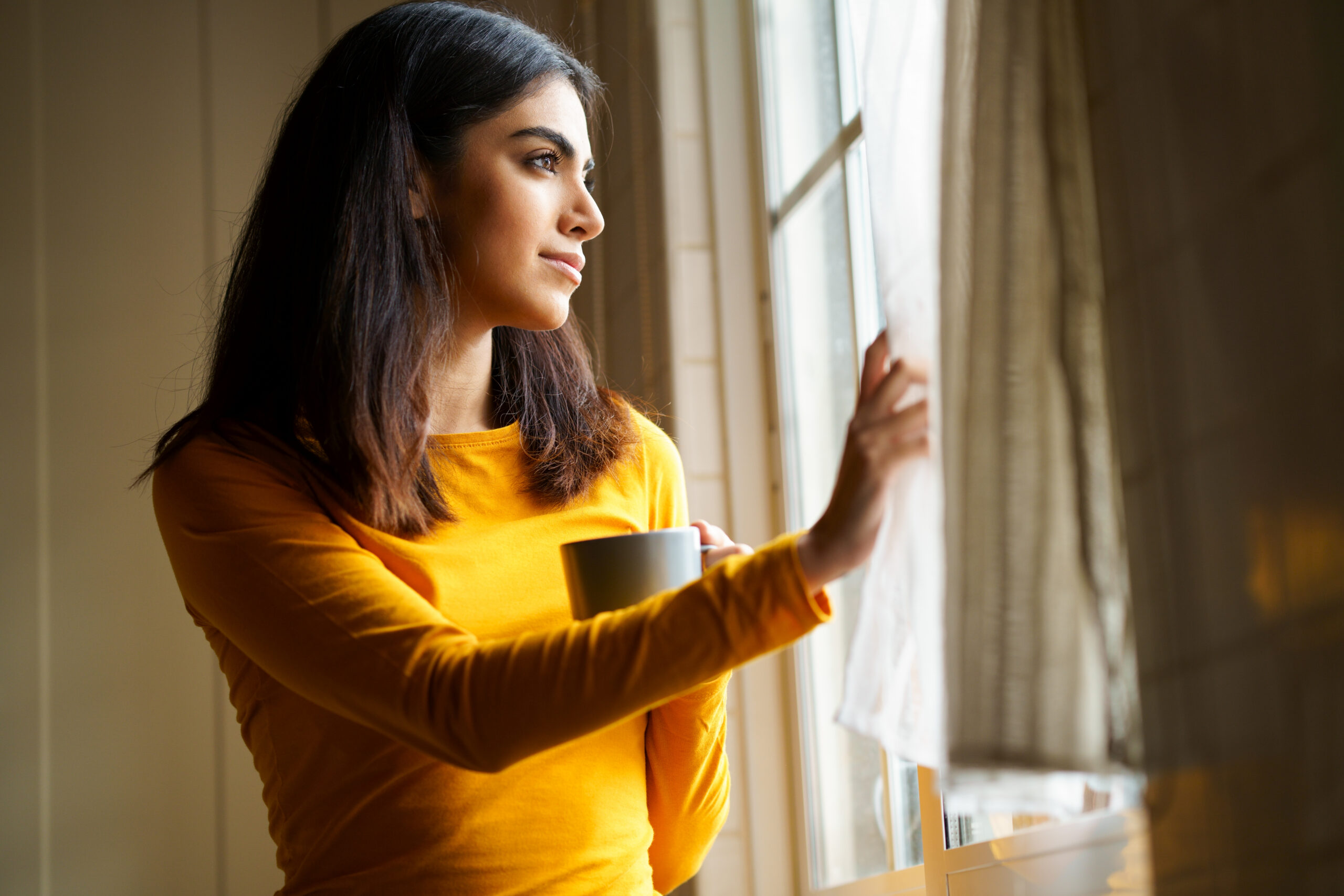 Mulher tomando café e olhando pela janela, representando o TDAH em mulheres e o diagnóstico tardio