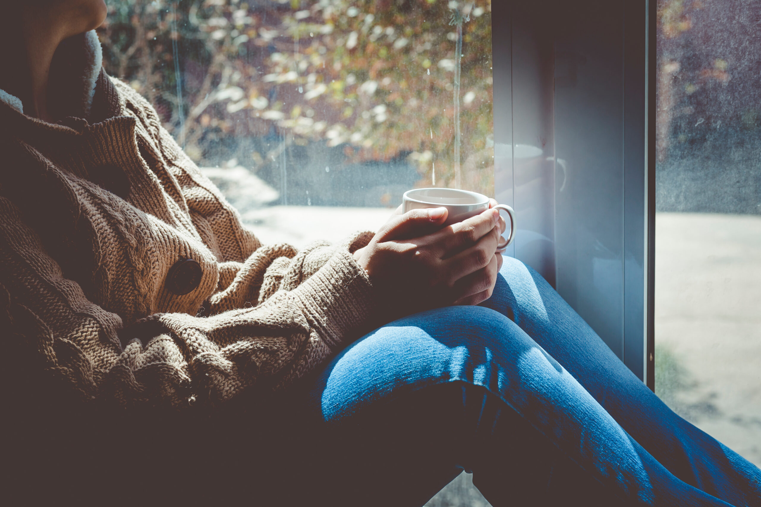 Pessoa com bebida quente junto à janela, ilustrando a depressão sazonal